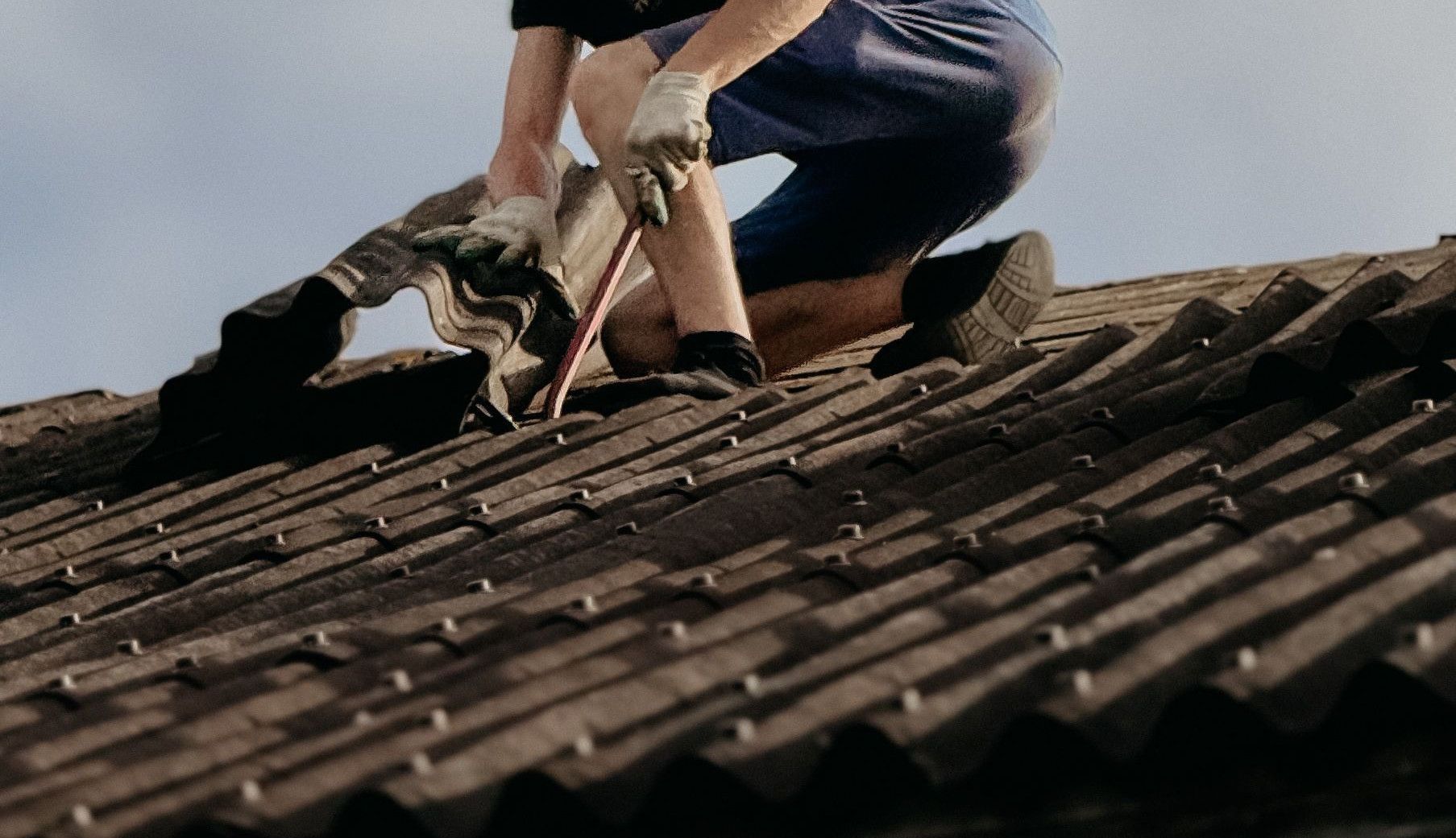 A construction worker with a safety helmet is repairing a roof outdoors during the day.